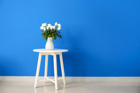 Beautiful vase with roses on table near color wallの写真素材