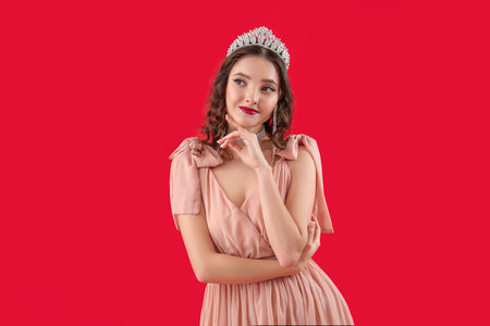 Beautiful young woman in prom dress and tiara on red backgroundの写真素材