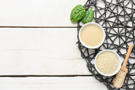 Composition with bowls of tasty tahini, sesame seeds and spinach on light wooden background