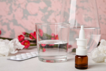 Nasal drops with glass of water on white table. Seasonal allergy conceptの写真素材
