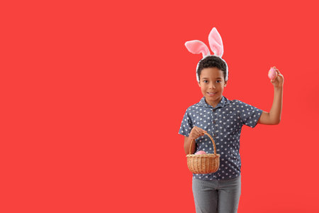 African-American little boy in bunny ears with basket of Easter eggs on red background