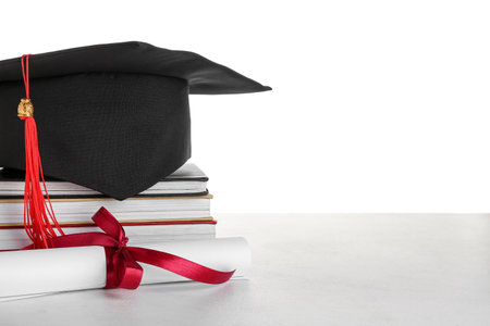 Graduation hat with diploma and books on table against white backgroundの写真素材