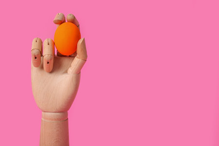 Decorative wooden hand with Easter egg on pink backgroundの写真素材