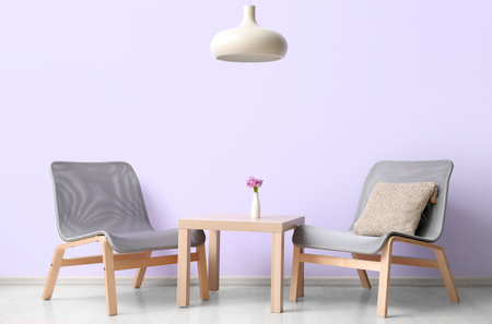Stylish gray armchairs and table near lilac wallの写真素材