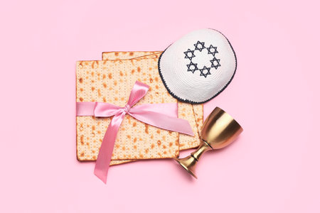 Jewish flatbread matza for Passover, kippah and cup on pink background