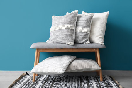Stylish decorative pillows on bench near blue wallの写真素材