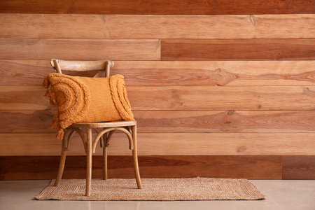 Stylish decorative pillow on chair near wooden wallの写真素材
