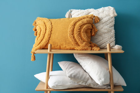 Stylish decorative pillows on shelving unit near blue wallの写真素材