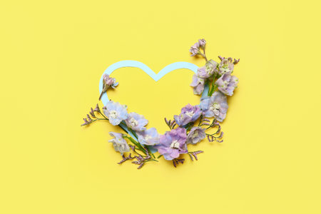 Blank heart-shaped frame and beautiful delphinium flowers on yellow backgroundの写真素材