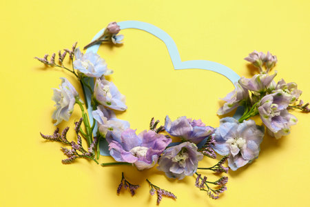Blank heart-shaped frame and beautiful delphinium flowers on yellow backgroundの写真素材