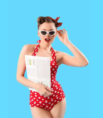 Young pin-up woman in swimsuit with newspaper on blue backgroundの写真素材