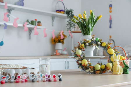 Vase with tulips, Easter wreath, rabbits and basket of eggs on table in kitchenの写真素材