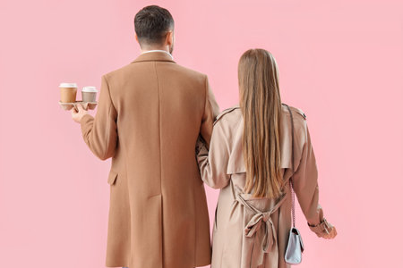 Young couple with cups of coffee on pink background, back viewの写真素材