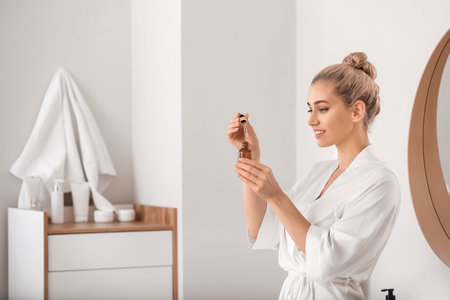 Beautiful young woman applying cosmetic oil in bathroomの写真素材