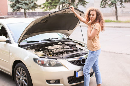 Stressed African-American woman near broken car outdoors