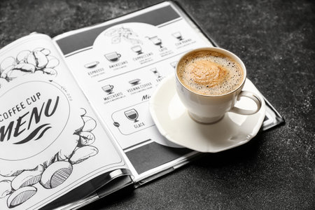 Cup of hot coffee and menu on table in cafeの写真素材