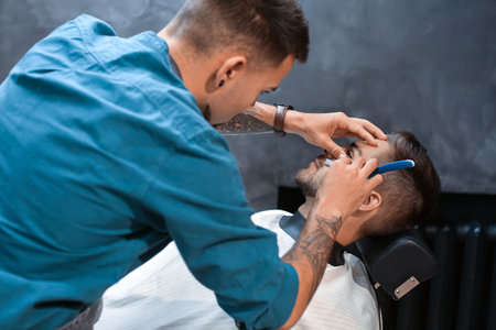 Hairdresser shaving client in barbershopの写真素材