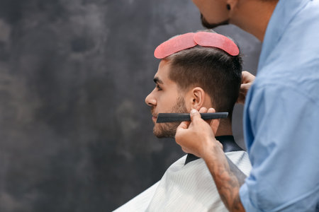 Professional hairdresser working with client in barbershopの写真素材