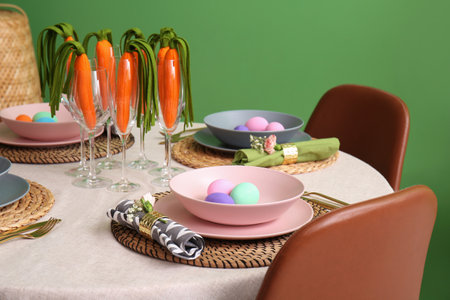 Stylish Easter table setting with decorative carrots near color wall, closeup