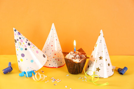 Birthday cupcake, party hats, whistles and confetti on color backgroundの写真素材