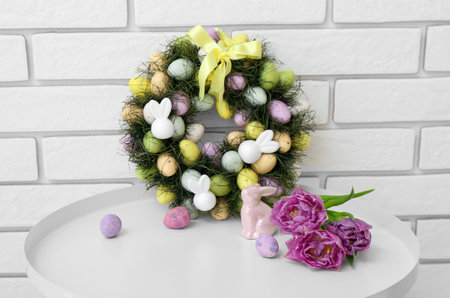 Easter wreath with rabbit and tulips on table near white brick wall
