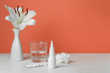 Nasal drops with pills, flower, glass of water and tissue on table near red wall. Seasonal allergy conceptの写真素材