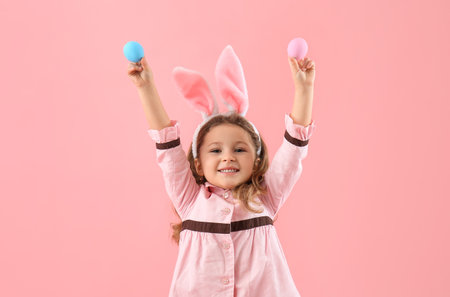 Cute little girl in bunny ears with painted Easter eggs on pink background