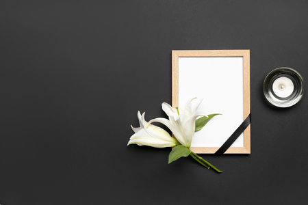 Blank funeral frame, lily flowers and burning candle on dark backgroundの写真素材