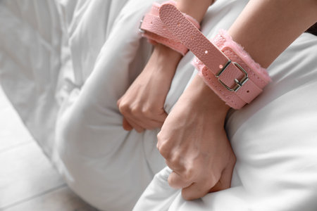 Woman with pink handcuffs on bed, closeupの写真素材