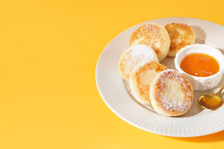 Plate with tasty cottage cheese pancakes and jam on yellow backgroundの写真素材