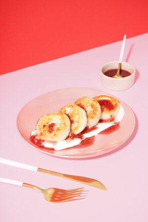 Plate of tasty cottage cheese pancakes with raspberry jam and sour cream on pink tableの写真素材