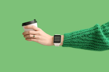 Woman with modern smartwatch and cup of coffee on green backgroundの写真素材