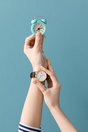 Woman with wristwatch and small alarm clock on blue backgroundの写真素材