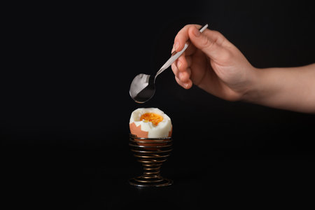 Woman with spoon and boiled egg on dark backgroundの写真素材