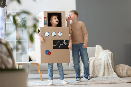 Little girl in cardboard robot costume playing with her brother at homeの写真素材