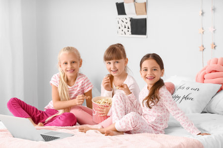 Cute little girls eating popcorn in bed at homeの写真素材