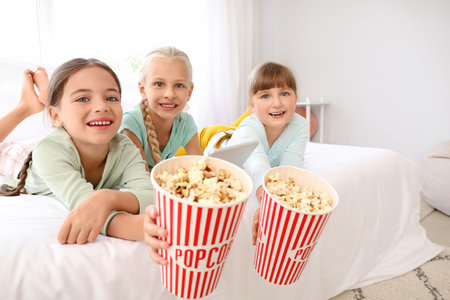 Cute little girls with tablet computer and popcorn at homeの写真素材