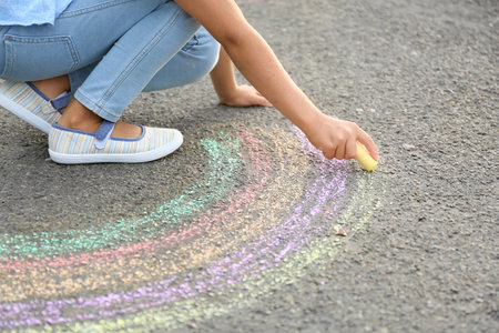 Little girl drawing rainbow with chalk on asphaltの写真素材