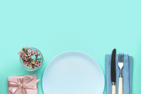 Table setting with gift box, cutlery and floral decor on turquoise backgroundの写真素材