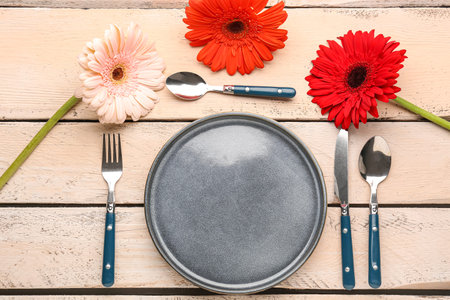 Table setting with beautiful gerbera flowers on beige wooden background