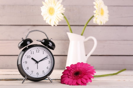 Alarm clock and beautiful gerbera flower on wooden background