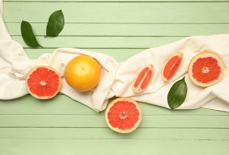 Composition with ripe grapefruits, napkin and plant leaves on color wooden background