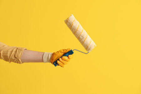 Worker with paint roller on yellow background