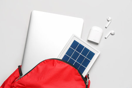 Bag with portable solar panel, laptop and earphones on light backgroundの写真素材