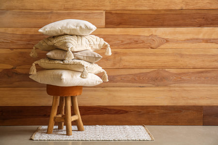 Stack of stylish decorative pillow on stool near wooden wallの写真素材