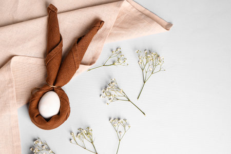 Composition with Easter egg wrapped in napkin and gypsophila flowers on light backgroundの写真素材