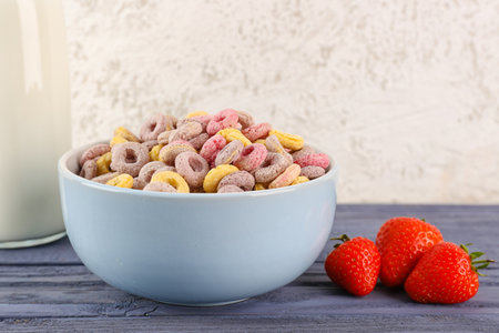 Bowl with colorful cereal rings and strawberries on blue wooden table near white grunge wallの写真素材