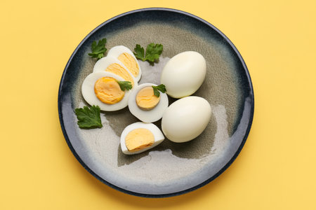 Plate with delicious boiled eggs and parsley on yellow backgroundの写真素材