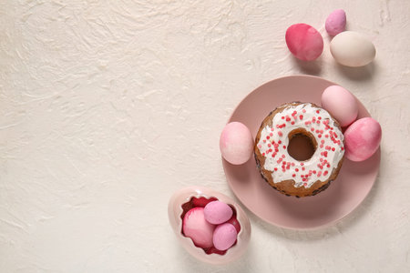 Plate with tasty Easter cake and painted eggs on light background