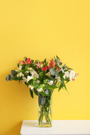 Vase with beautiful alstroemeria flowers on table near yellow wallの写真素材